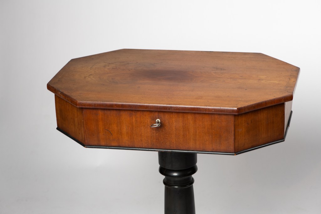 Octagonal wooden sewing table with a drawer and a black pedestal base.