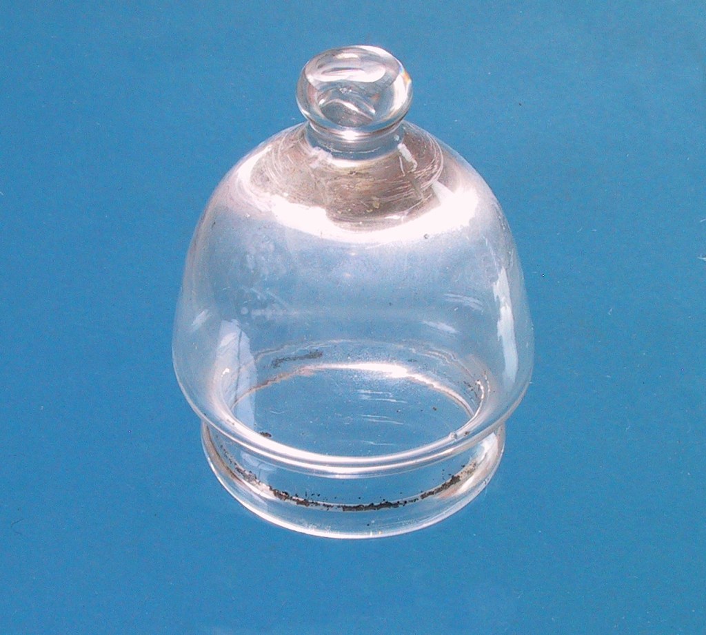 Eit klart glasstykke med kuppelforma, ståande på ein blå bakgrunn.
