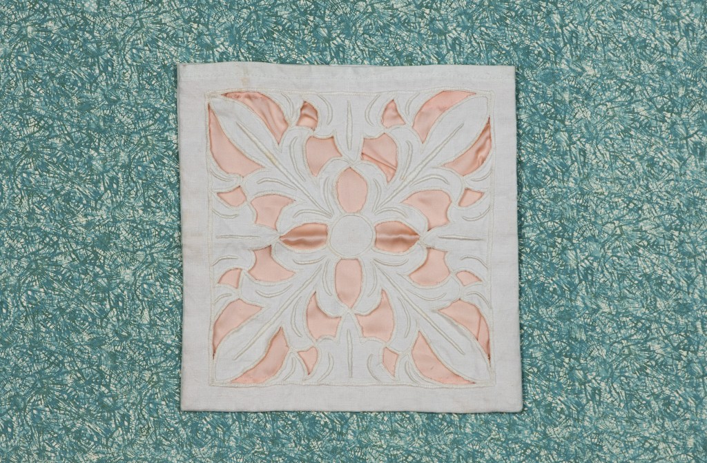 Eit broderi med lys rosa mønster på ein lyseblå bakgrunn.