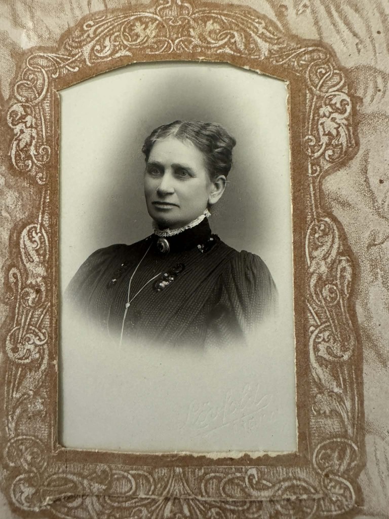 Portrett av ei kvinne frå tidleg 1900-tall, med oppsatt hår og mørk kjole, innramma i ei utsmykka ramme.